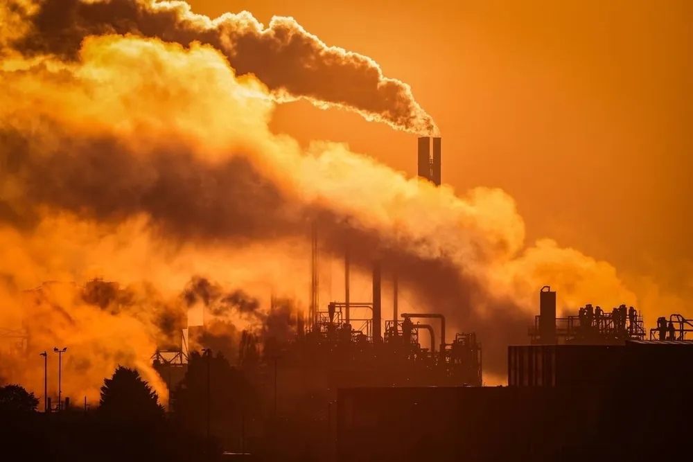 Industrial smokestacks releasing emissions against an orange sky
